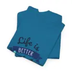 Two teal blue t-shirts folded and stacked showing partial 'Life is BETTER' text from lake-themed graphic design against white background