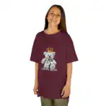 Child wearing an oversized burgundy t-shirt with teddy bear crown graphic and 'TEDDY BEAR' text, paired with olive green pants, smiling at camera against white background