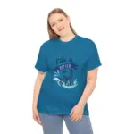 Woman with head tilted smiling while wearing teal blue t-shirt featuring 'Life is Better at the Lake' graphic with wave and boat design, paired with light blue jeans against white background