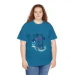 Woman facing forward wearing teal blue oversized t-shirt with 'Life is Better at the Lake' graphic featuring wave splash and boat design, styled with light blue jeans against white background
